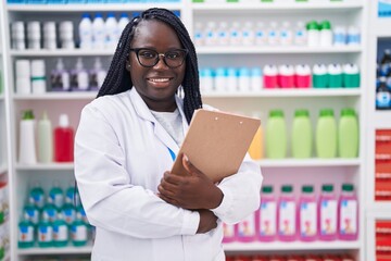 African american woman pharmacist smiling confident holding clipboard at pharmacy