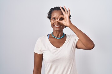 African woman with dreadlocks standing over white background doing ok gesture with hand smiling, eye looking through fingers with happy face.
