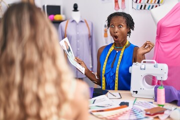 African woman with dreadlocks dressmaker designer at atelier with customer scared and amazed with open mouth for surprise, disbelief face - obrazy, fototapety, plakaty