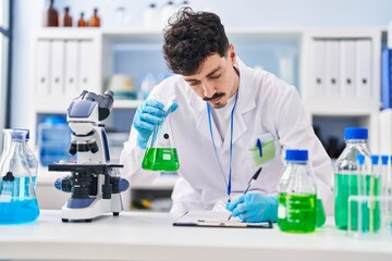 Fototapeta premium Young caucasian man scientist writing report holding test tube at laboratory