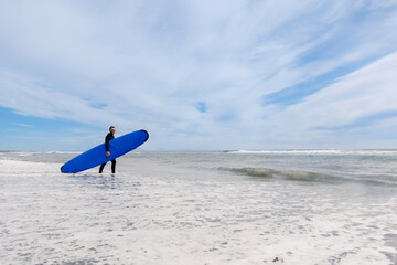 Happy man surfer with blue surfboard in wetsuit surfing in ocean on spot Kamchatka Russia, sunlight. Lifestyle adventure winter sport