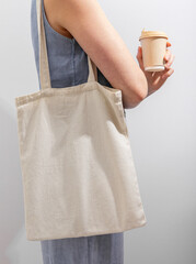 Shopper on shoulder and paper cup, takeaway coffee in hand. Woman carrying eco tote bag mockup