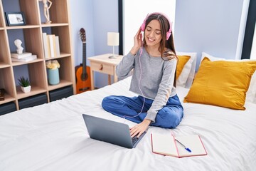 Young beautiful hispanic woman student listening vto music studying on bed at bedroom