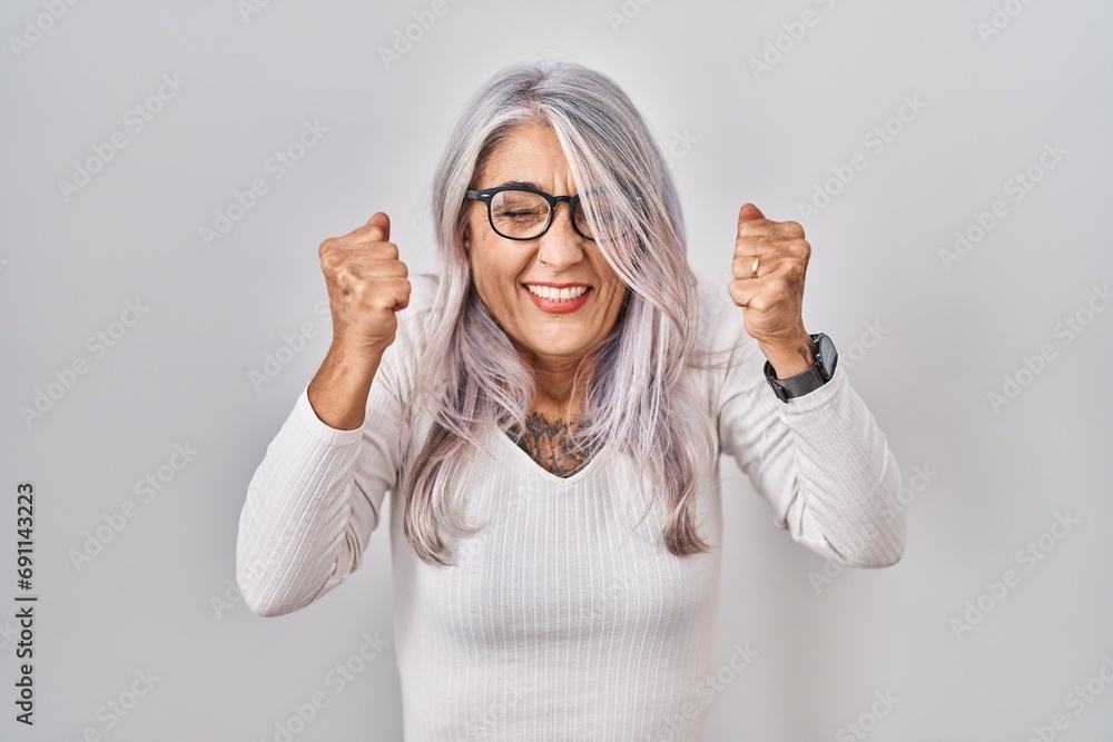 Wall mural middle age woman with grey hair standing over white background excited for success with arms raised 