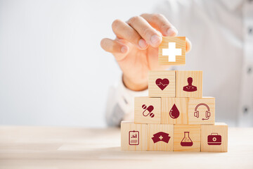 Wooden block held by hand showcases healthcare and medical icons. Conveys safety, health, and...