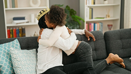 African american father and daughter wearing king crown kissing hand hugging each other at home - obrazy, fototapety, plakaty