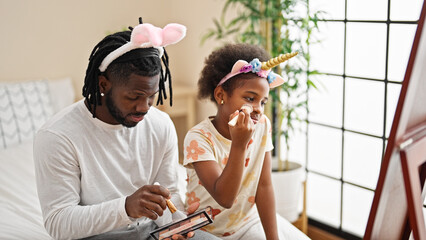 African american father and daughter wearing funny diadem applying makeup looking on mirror at...