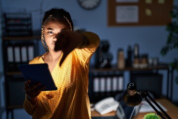 African american woman with braids working at the office at night with tablet looking unhappy and...