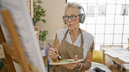 Elderly grey-haired woman artist absorbed in the joy of painting, surrounded by paintbrushes and...