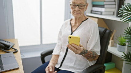 Elegant, grey-haired senior woman boss, concentrating at work, seriously typing messages on...