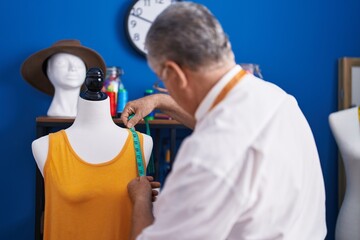 Middle age grey-haired man tailor measuring dress at tailor shop