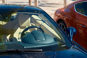Two expensive sports cars stand side by side in sunny weather, a view of the bright interior through any glass