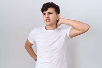 Young non binary man wearing casual white t shirt suffering of neck ache injury, touching neck with...