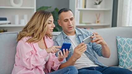 Man and woman couple using smartphones sitting on sofa at home