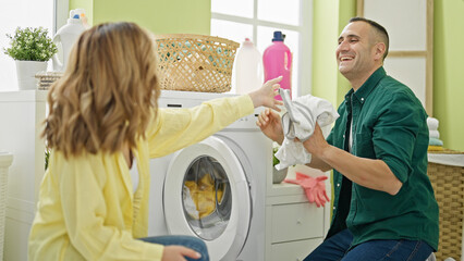 Man and woman couple washing clothes together smiling at laundry room