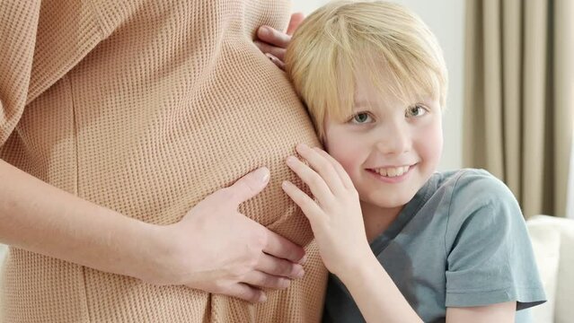 A schoolboy boy hugging and listening belly of his pregnant mother. Pregnant mother and her eldest child at home. Future big brother. Siblings