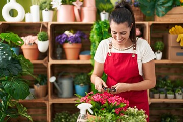 Young beautiful hispanic woman florist cutting plants at flower shop