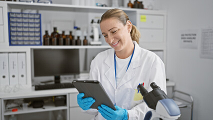 Blonde woman scientist's jubilant smile at the lab, young and confident, enjoying her touchpad...