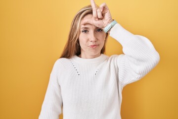 Young caucasian woman wearing white sweater over yellow background making fun of people with...
