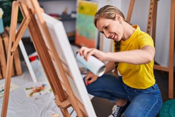 Young blonde woman artist smiling confident using graffiti spray drawing at art studio
