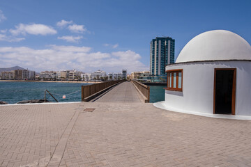Fototapeta na wymiar View of the city of Arrecife from the Fermina islet, from a wooden bridge with a white guardhouse. Turquoise blue water. Sky with big white clouds. Seascape. Lanzarote, Canary Islands, Spain.