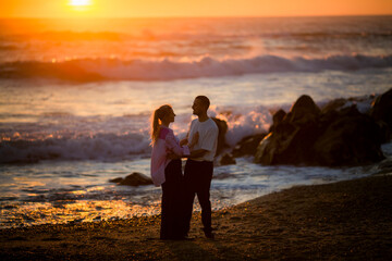 Fototapeta premium A young couple on the beach embrace during a golden sunset.