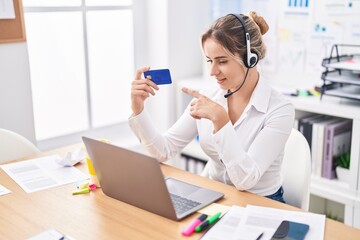 Young blonde woman call center agent holding credit card working at office