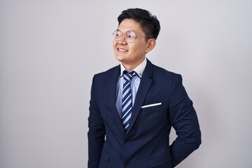 Young asian man wearing business suit and tie looking away to side with smile on face, natural...