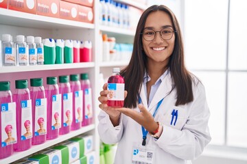 Young hispanic woman working at pharmacy drugstore holding syrup smiling with a happy and cool smile on face. showing teeth.