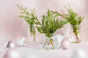 Still life from Cypress branches in transparent vases with Christmas decorations. Bouquet with evergreen spruce and balls on light beige background. Minimalist Christmas decor in in pastel colors
