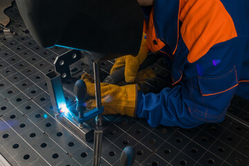 a worker welds an iron structure on a table
