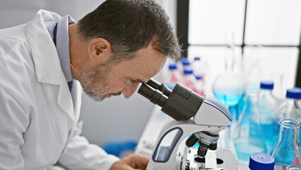 Aged man with grey hair, a scientist busy in his lab, peering into microscope for medical discovery