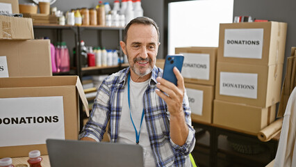 Middle age man with grey hair volunteer having video call by smartphone at charity center