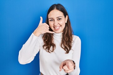 Young hispanic woman standing over blue background smiling doing talking on the telephone gesture...