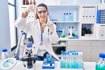 Young hispanic woman working at scientist laboratory smiling making frame with hands and fingers with happy face. creativity and photography concept.