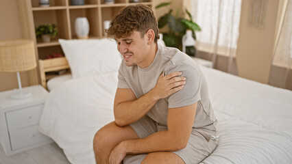 Worried young hispanic man, in pyjamas, suffering intense shoulder pain. unhappy, he lies awake in...
