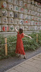 Naklejka premium Beautiful hispanic woman smiling, standing by shake barrels at meiji temple while embracing japanese culture, all while donning glasses