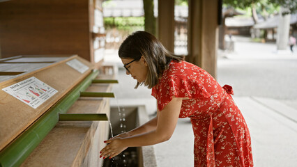 Beautiful hispanic woman with glasses participates in traditional asian purifying ritual at meiji...