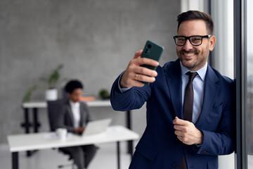 Well dressed businessman taking selfie with smartphone in office