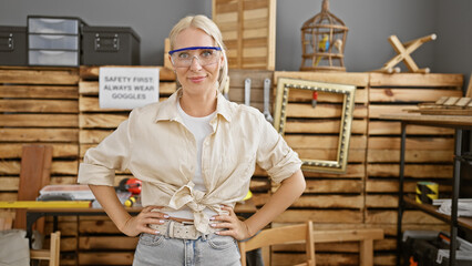 Vibrant, young blonde woman carpenter, beaming with professionalism, ensuring safety with security glasses at her carpentry workshop.