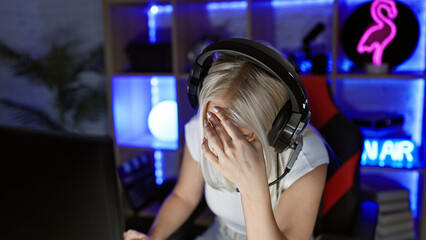 Overworked and stressed young blonde female streamer battling stress while gaming late night in a...