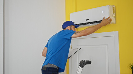 Young hispanic man technician repairing air condition machine holding clipboard at home