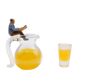 miniature man reading a newspaper sitting on a jug of orange juice