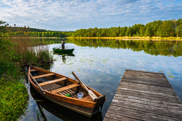 POSTAWELE, POLAND - MAY 20, 2023: Wooden fishing boat anchoring at pier on calm water lake at...
