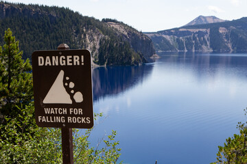 Danger Watch for Falling Rocks sign overlooking Crater Lake in Crater Lake National Park with deep...