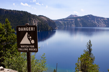 Danger Watch for Falling Rocks sign overlooking Crater Lake in Crater Lake National Park with deep...