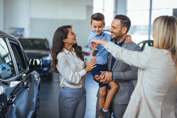 Young happy family enjoying while buying a new car in a showroom. Saleswoman at car dealership...