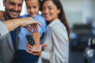 Happy parents with small kid after receiving keys for their new car in a showroom. Congratulations,...