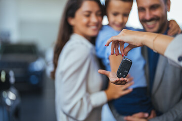 Happy parents with small kid after receiving keys for their new car in a showroom. Congratulations, we have a deal about buying a car! Happy family came to an agreement with a car salesperson - Powered by Adobe