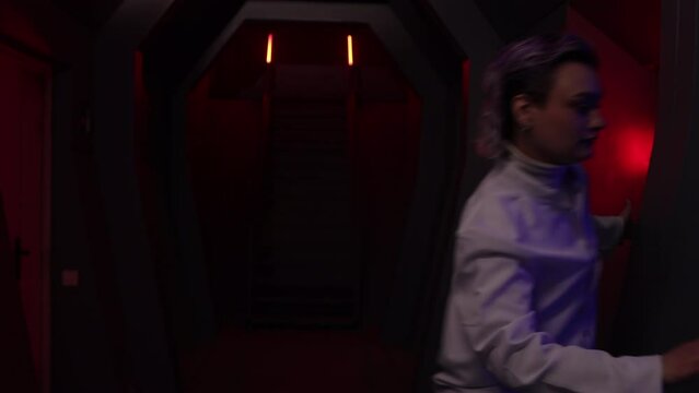 Man and woman in white uniform running along red lights corridor of futuristic design interior. Stressed and worried professionals looking annoyed as they heard an alarm. High quality 4k footage